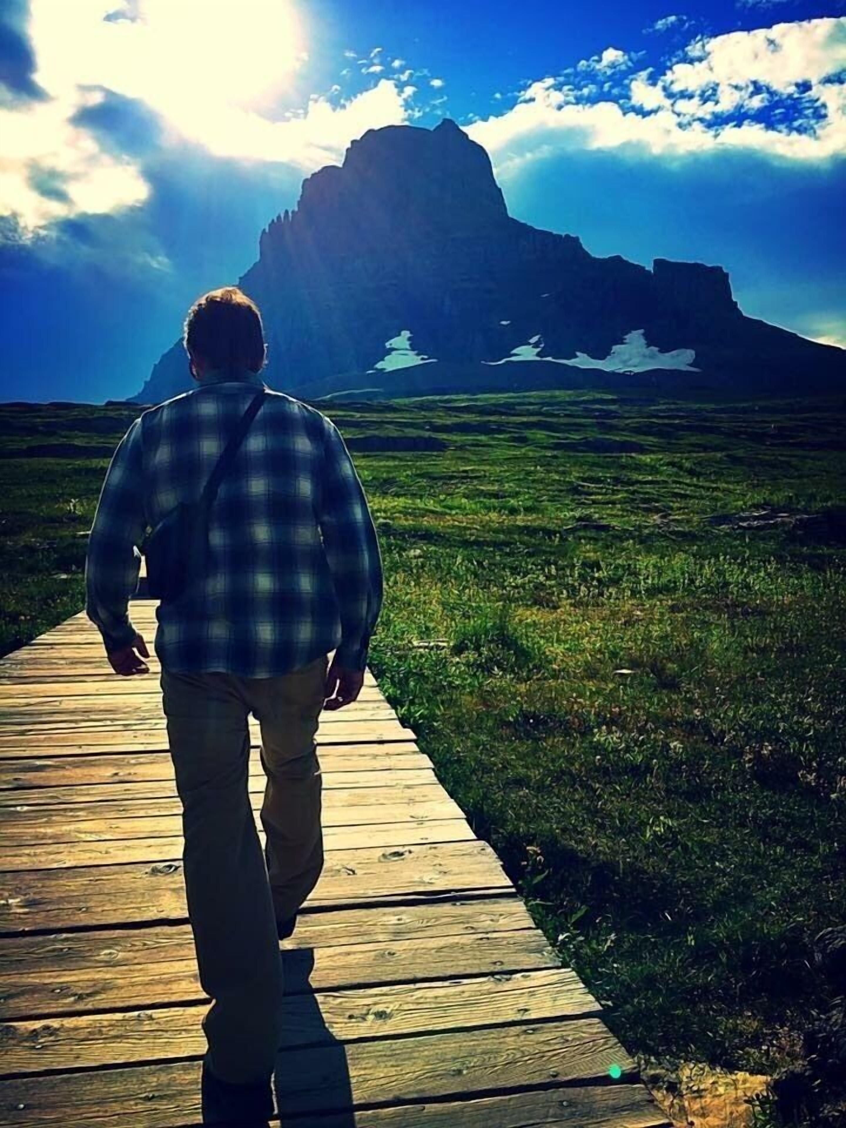 Una persona camina sobre una pasarela de madera hacia una montaña.
