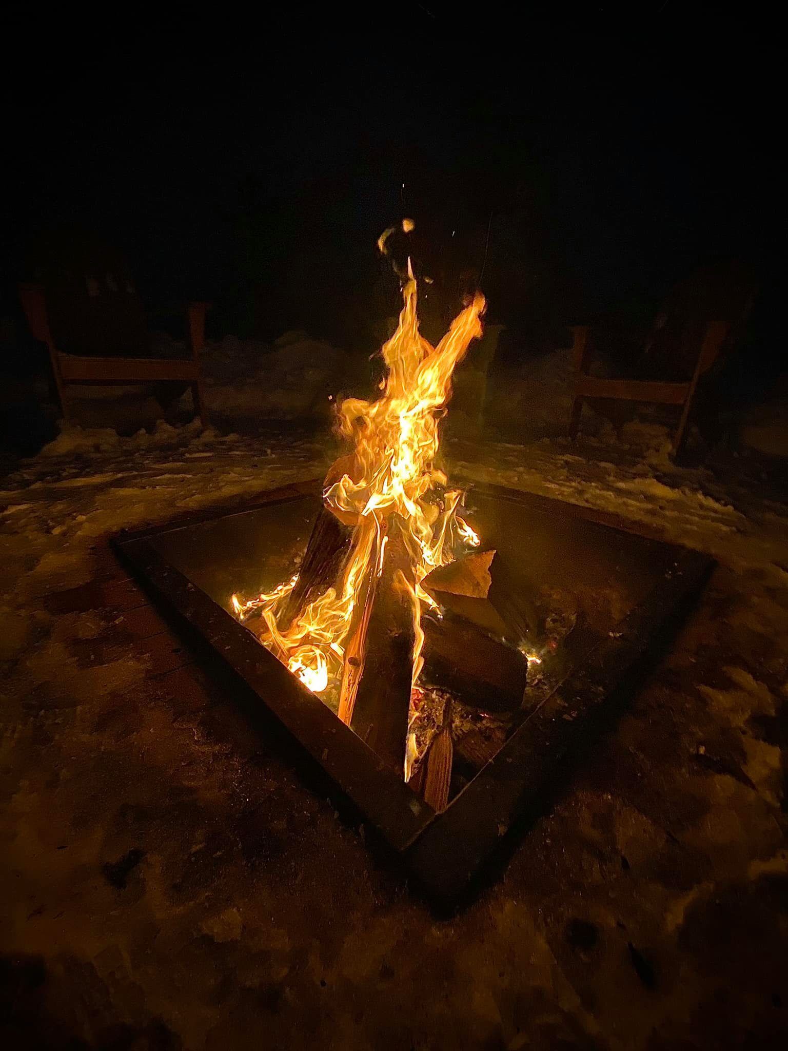 A campfire in a metal fire pit surrounded by snow.
