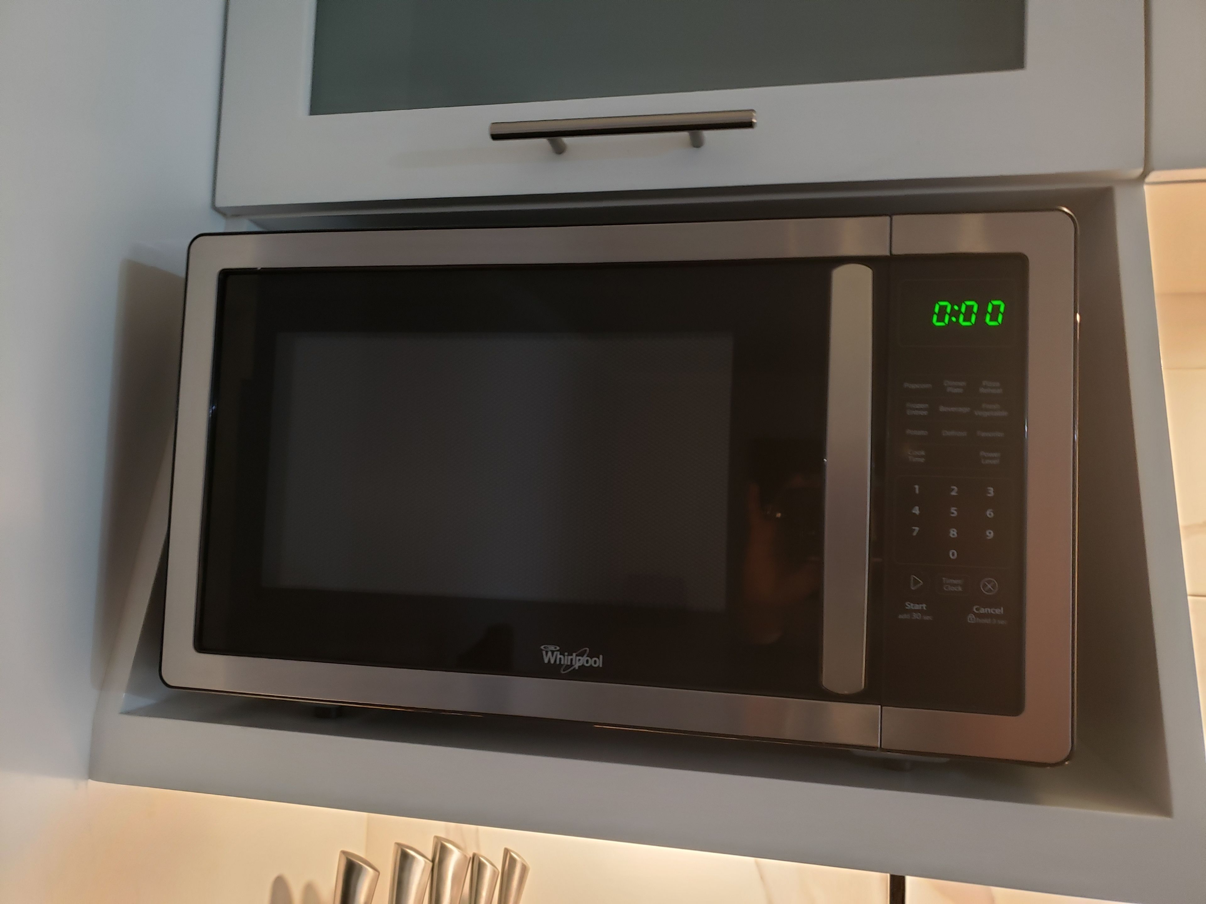 Whirlpool-merkkinen mikroaaltouuni, jossa on digitaalinen näyttö ja ohjauspaneeli, ja joka on asennettu keittiön työtasolle.