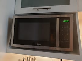 Whirlpool-merkkinen mikroaaltouuni, jossa on digitaalinen näyttö ja ohjauspaneeli, ja joka on asennettu keittiön työtasolle.
