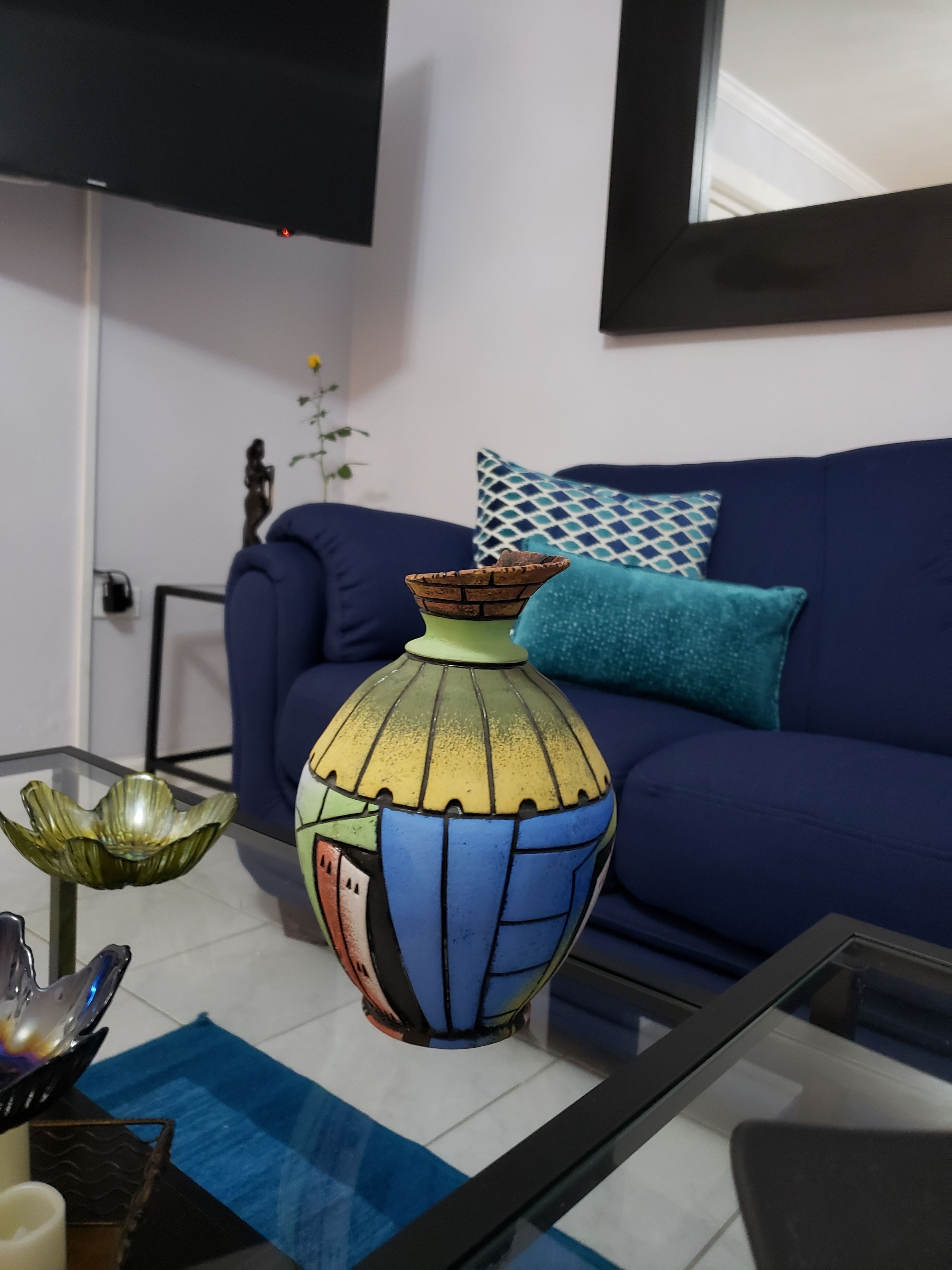 Un salon avec un canapé bleu, un vase coloré et une table basse en verre.