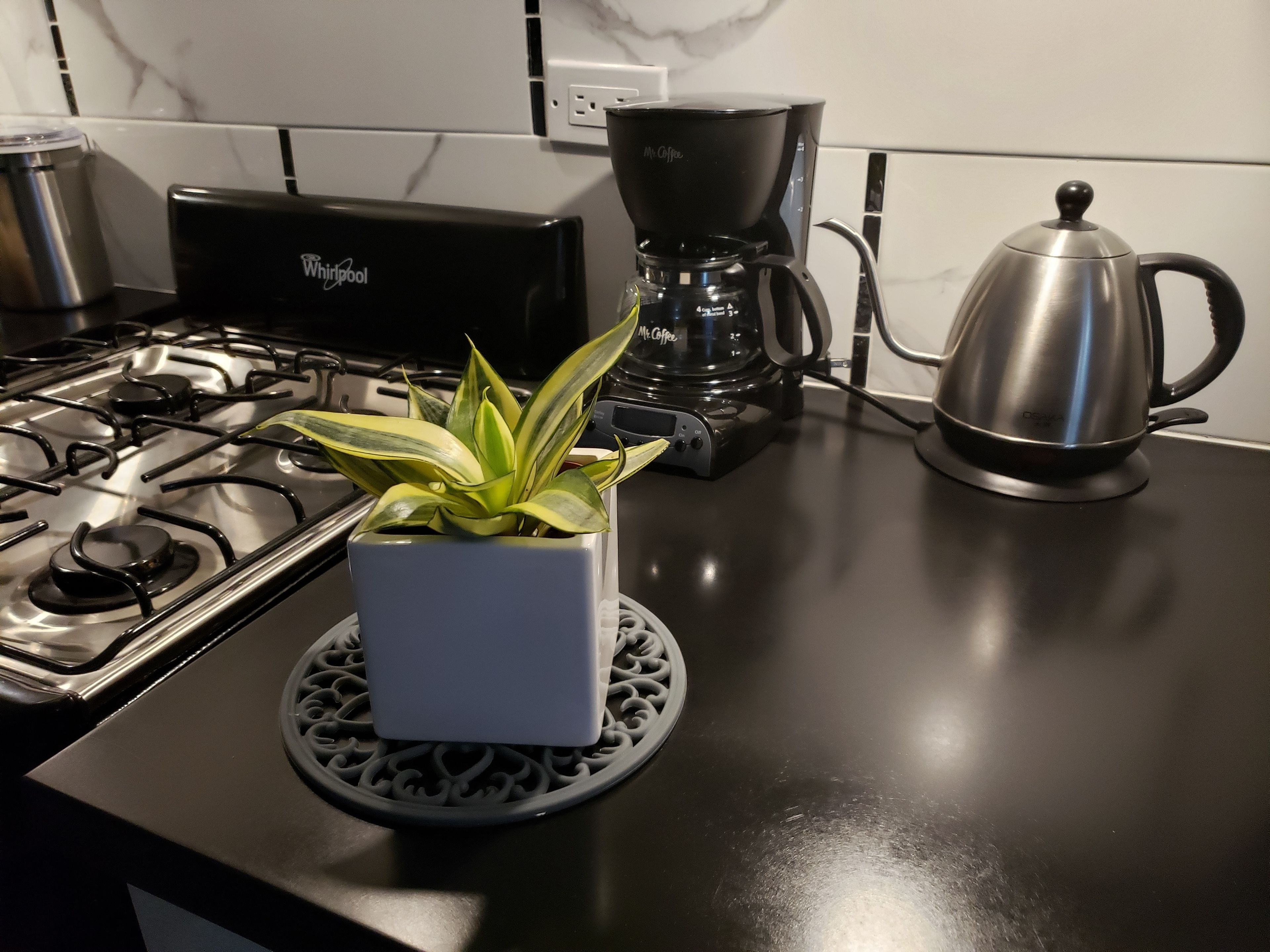 Keittiössä on Whirlpool-merkkinen liesi, kahvinkeitin ja ruostumattomasta teräksestä valmistettu vedenkeitin, jotka ovat työtasolla.
