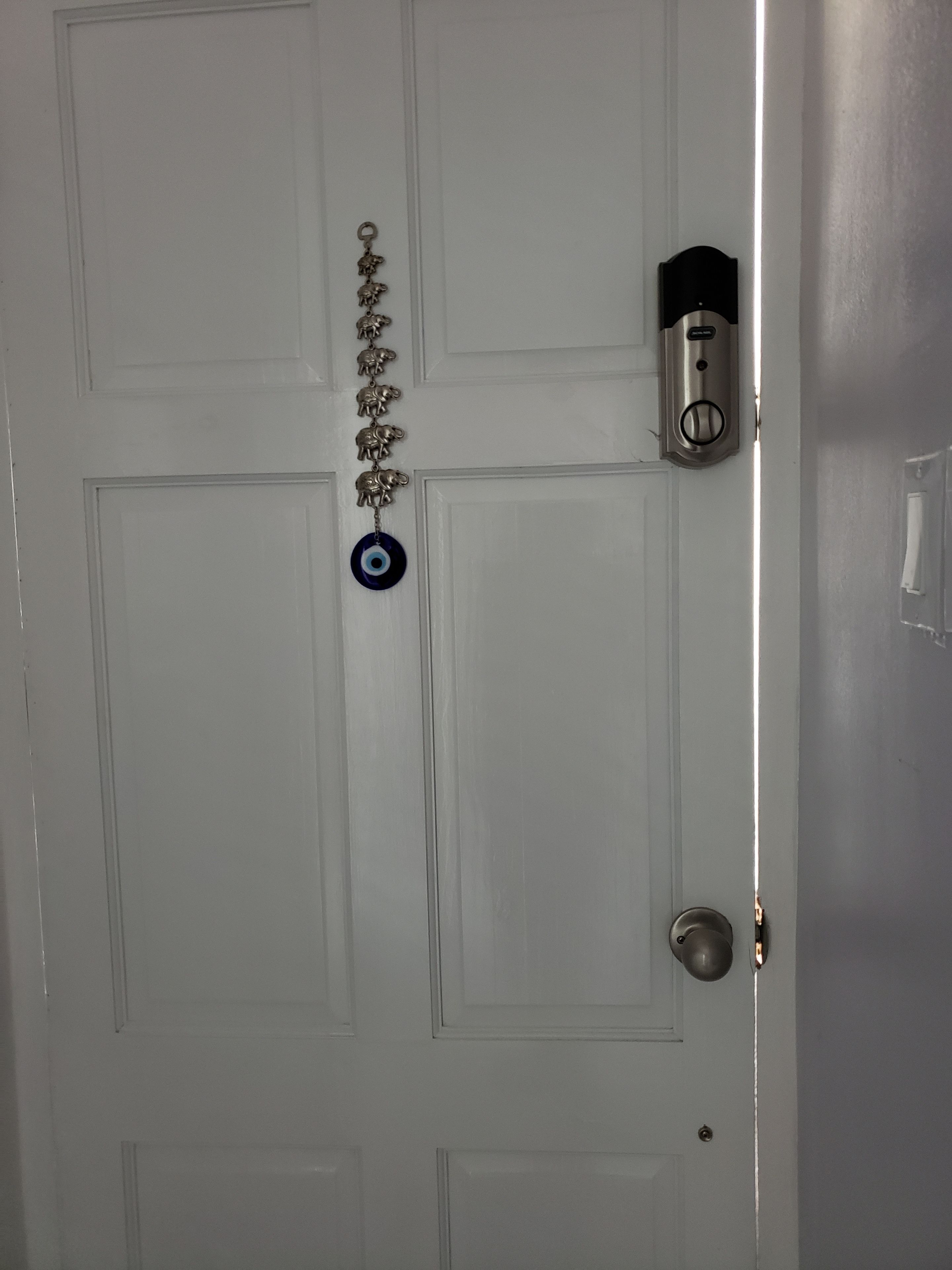 Una puerta blanca con un ojo de cerradura, un timbre y una cadena decorativa de metal con figuras de animales.
