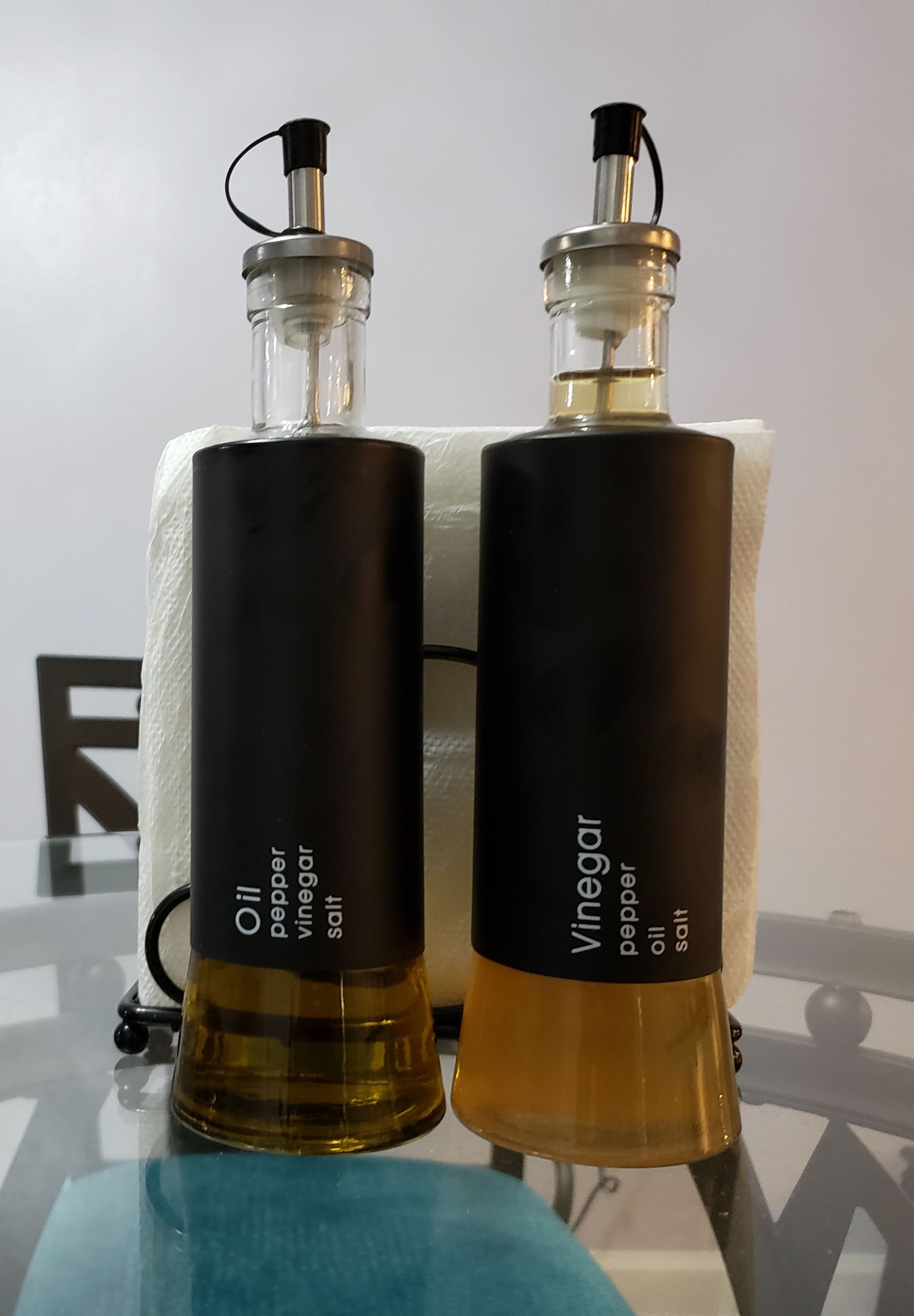Two bottles of vinegar on a glass table against a white wall.