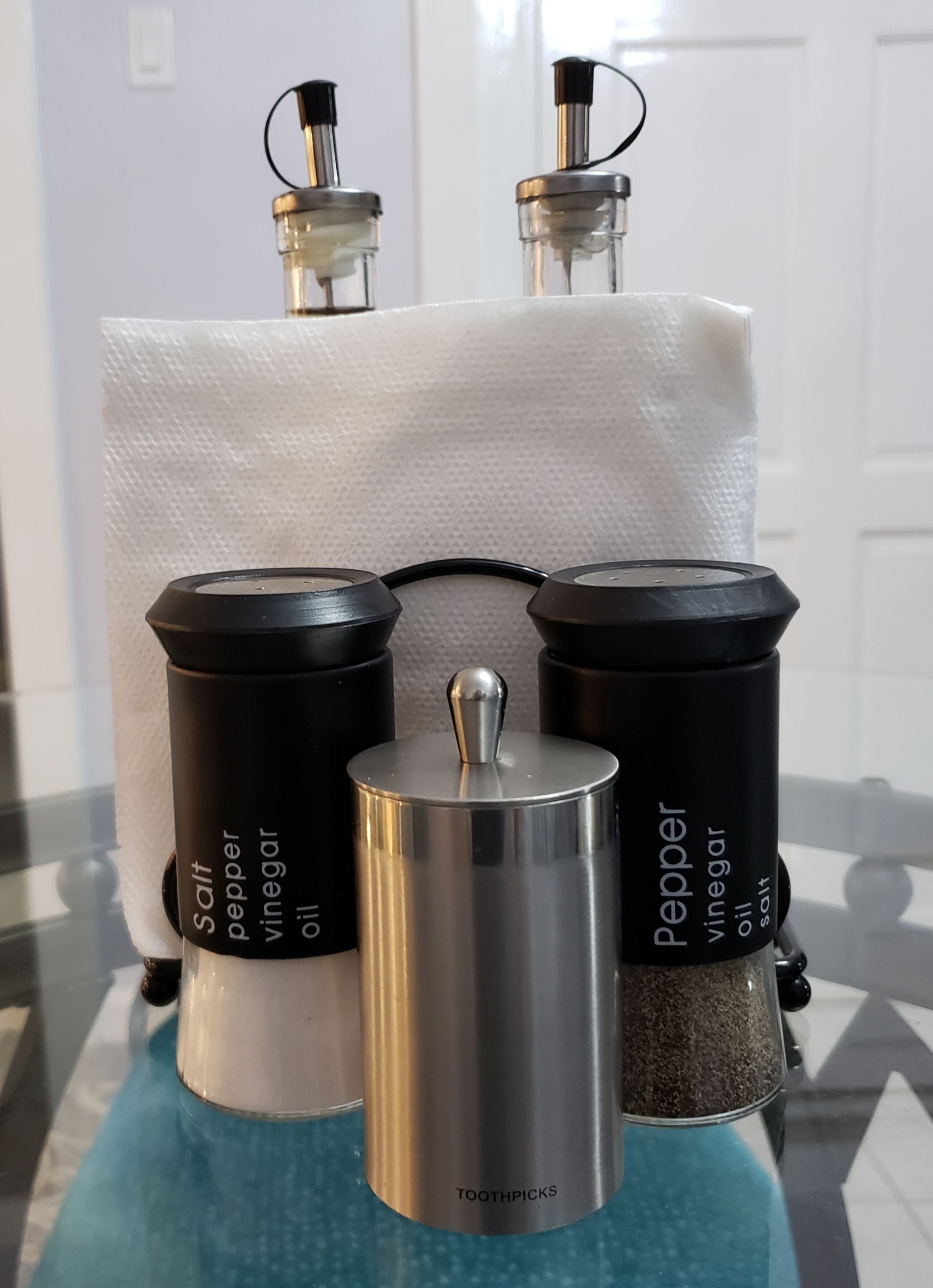 A kitchen counter with four containers labeled with different condiments: salt, pepper, vinegar, and oil.