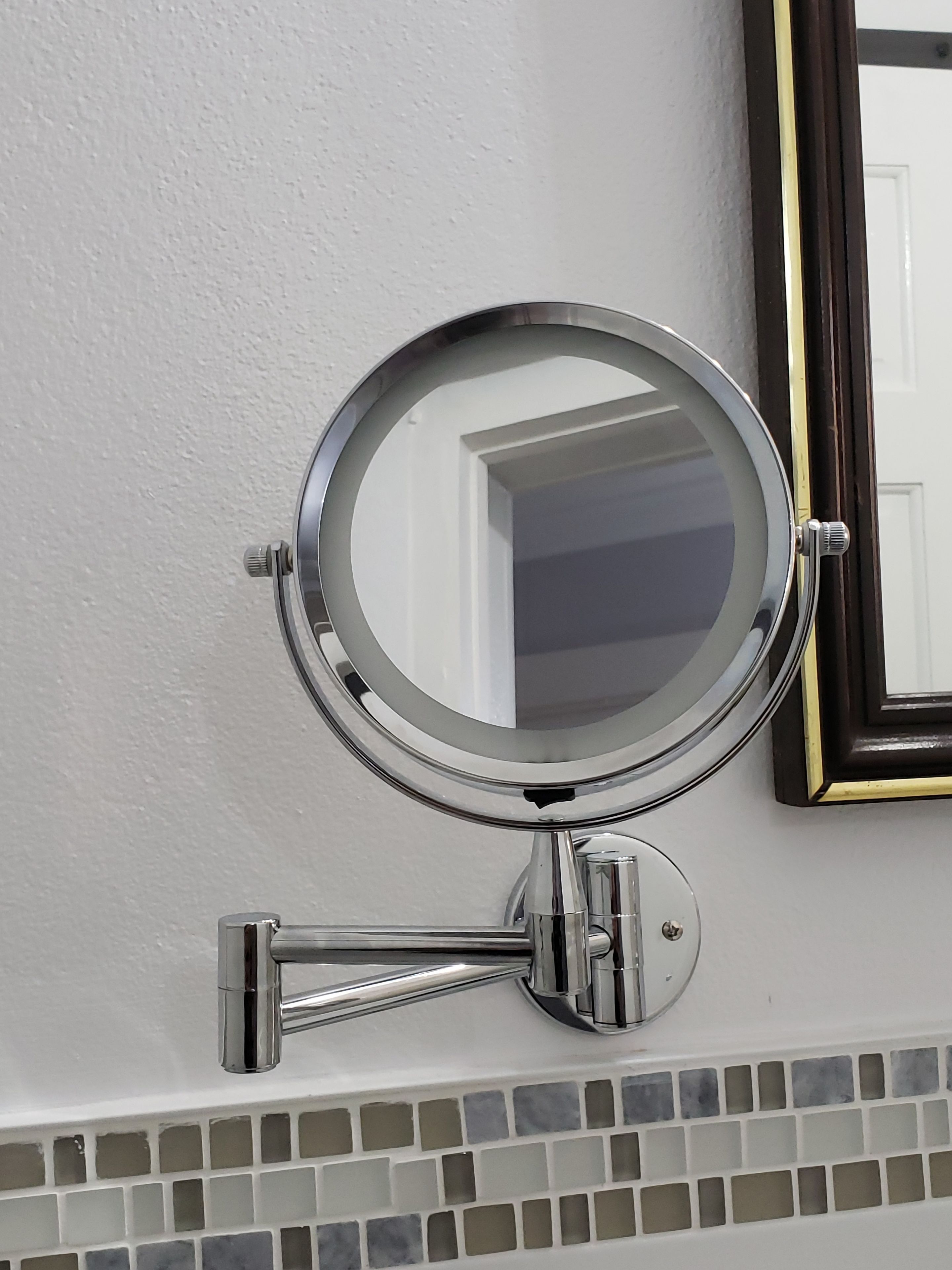 A wall-mounted mirror with a chrome finish, a door frame, and a tiled backsplash.