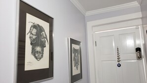 A hallway with two framed black and white portraits on the wall, a white door with a keypad lock, and a small decorative item hanging on the door. - Millsborough B&B (Kingston)