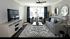 Un salon équipé d’un téléviseur à écran plat, d’un ventilateur de plafond, d’un canapé, d’une table basse et d’un grand tapis.