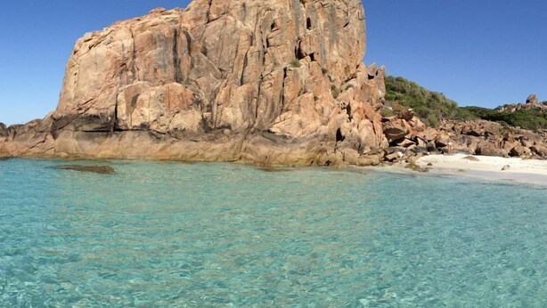 Costa rocosa con agua turquesa cristalina y una gran formación rocosa.