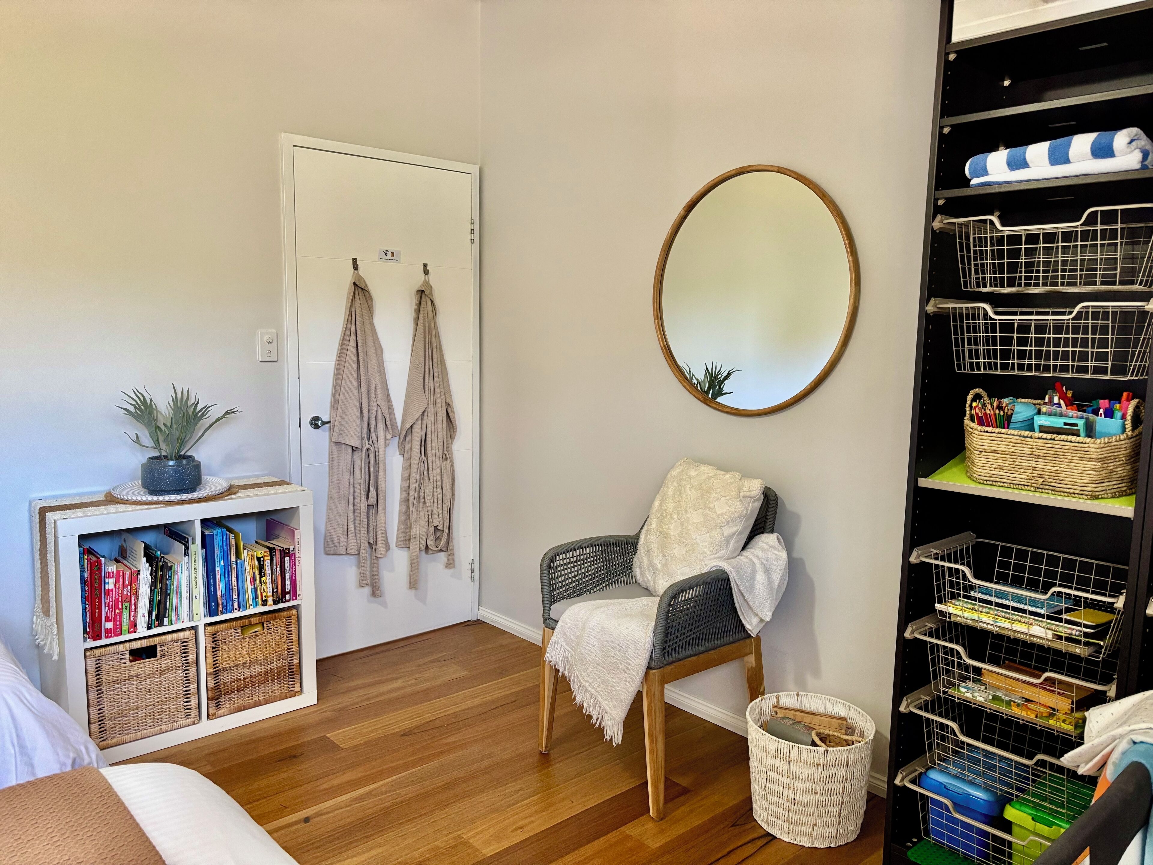 A room with a bookshelf, a chair, a mirror, and a storage unit.