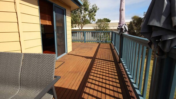 A wooden deck with a blue railing, a sliding glass door, and a gray chair. - Pegasus Retreat - in the coastal village of Venus Bay (Venus Bay)