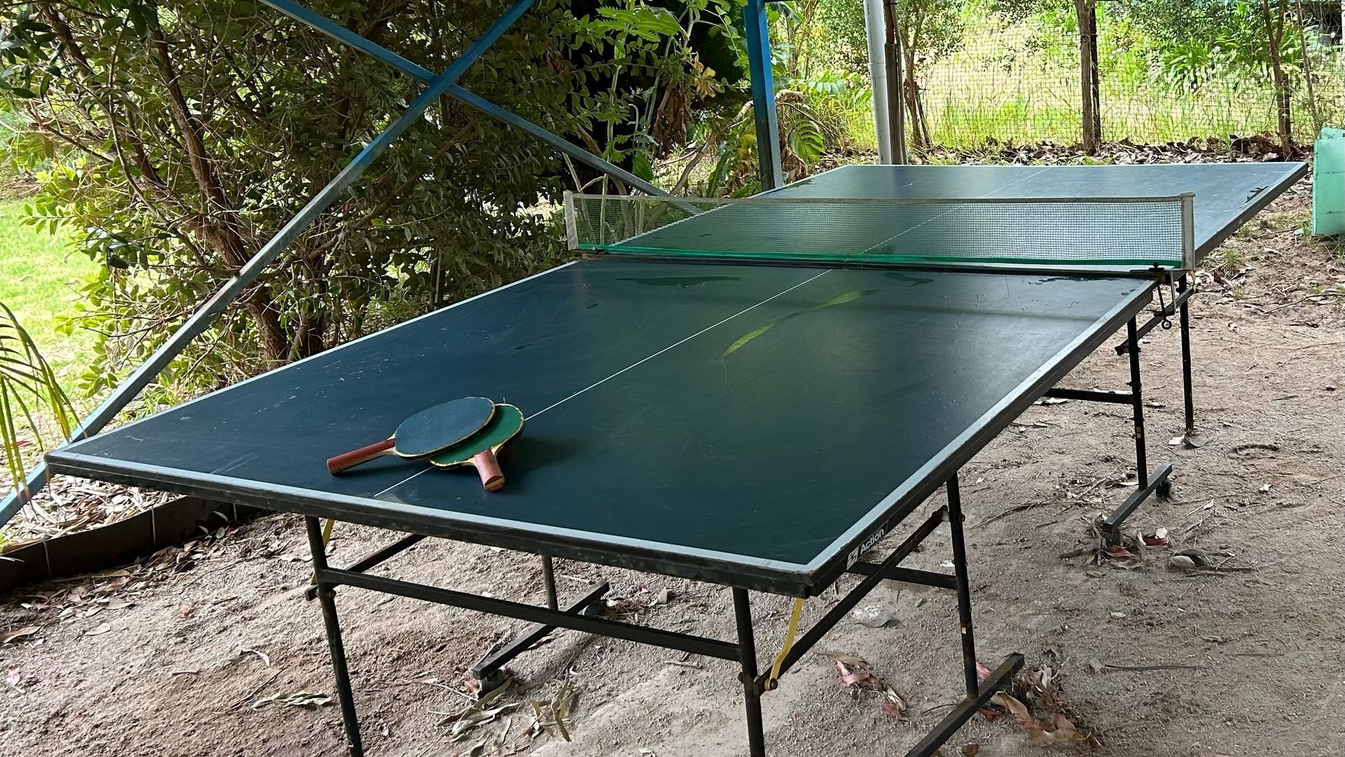 Ein Tischtennis-Tisch mit zwei Schlägern, draußen aufgestellt, mit Metallgestell und grüner Spielfläche.
