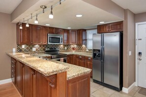 Una cocina con armarios de madera, encimera de granito, electrodomésticos de acero inoxidable e iluminación colgante.