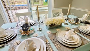 A dining table set for a meal with white plates, silverware, and glassware, decorated with white flowers and a candle. - Private Heated Pool • 5BR/3BA • Near Beaches and Nickerson Park (Brewster)
