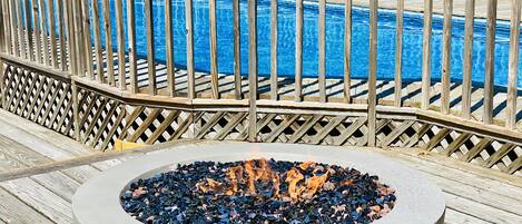 A poolside area with a fire pit and a wooden deck.