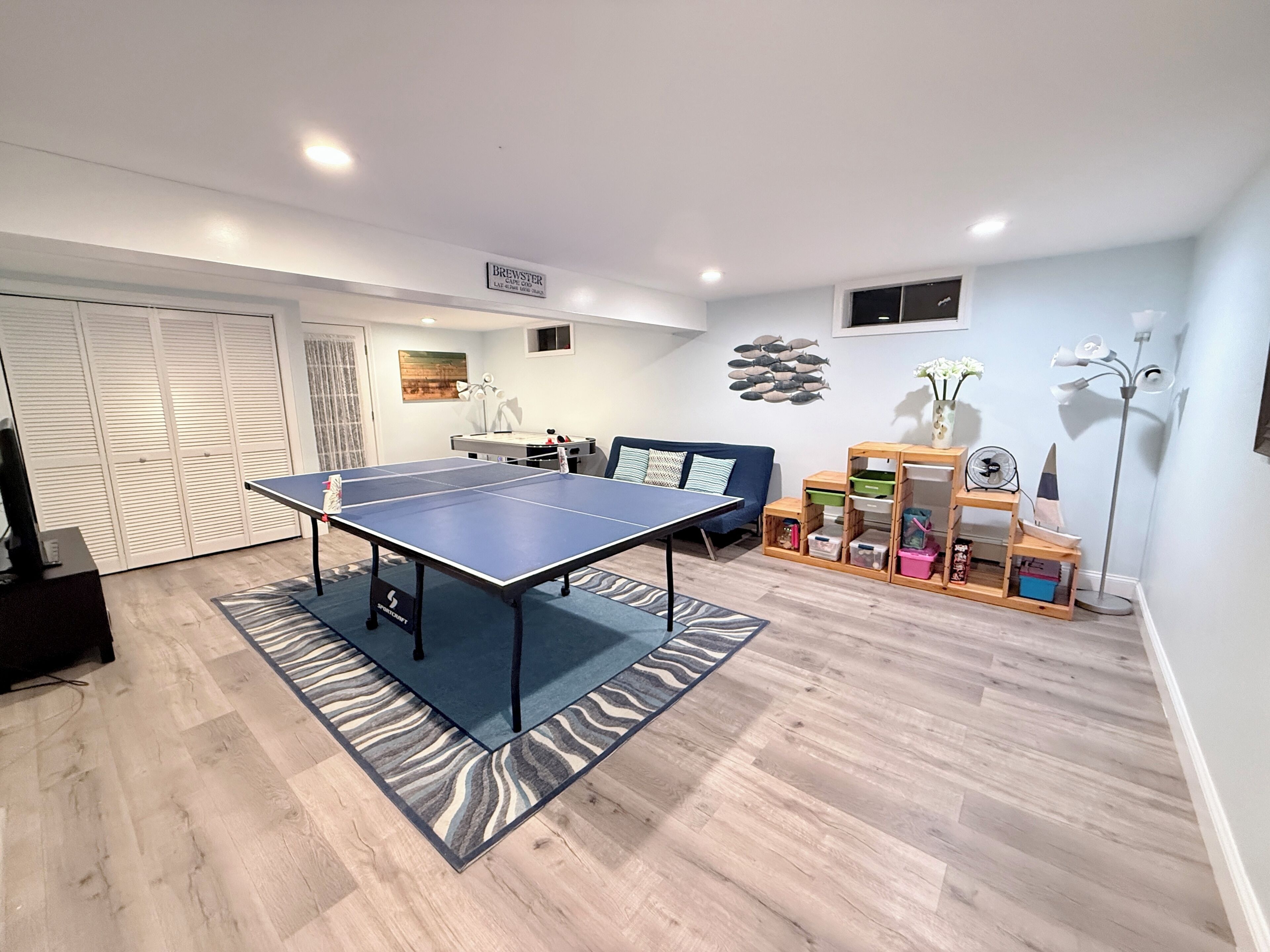 Una habitación con mesa de ping pong, sofá, escritorio y estantería.