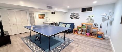 Una habitación con mesa de ping pong, sofá, escritorio y estantería.
