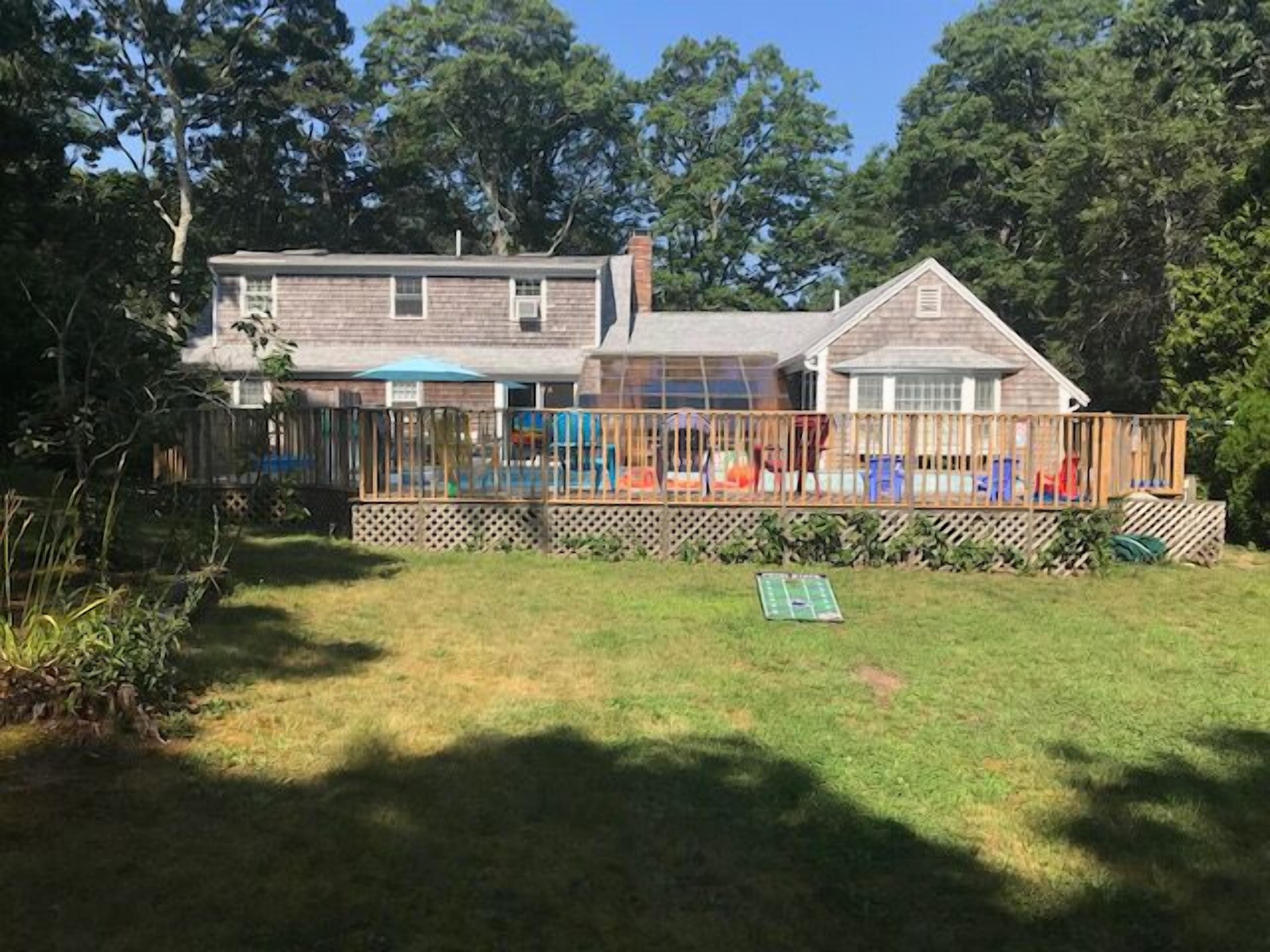 Una casa de dos plantas con un deck cercado y un patio cubierto de césped.