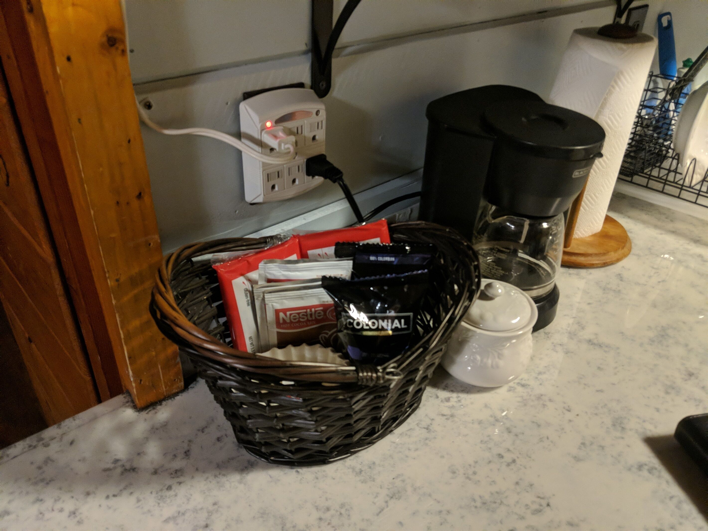 En köksbänk med en korg som innehåller kaffekapslar, en kaffebryggare och en glaskanna.