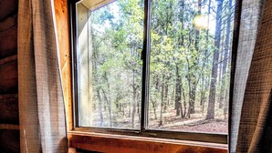 Ein Blockhauszimmer mit großem Fenster und Blick auf einen Wald.