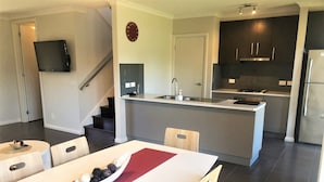 A modern kitchen with dark cabinetry, a central island with a sink, and a dining area with a red runner table.