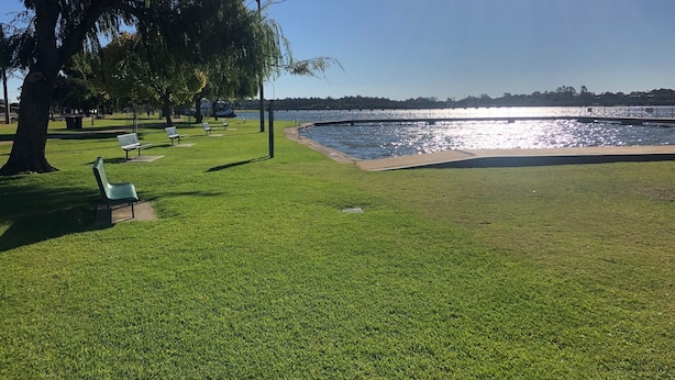 A park with green grass, benches, and a body of water.