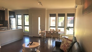 A modern living room with a black leather sofa, a round coffee table, and a dining area with a table and chairs.