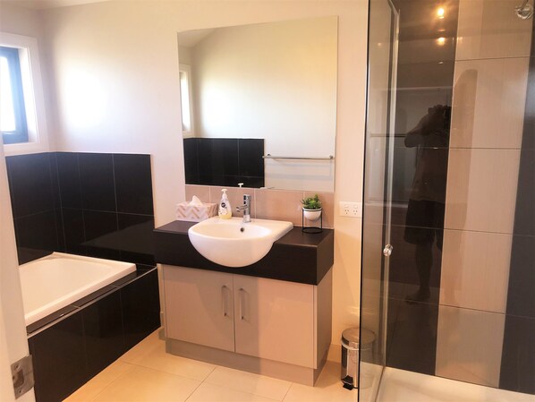 Une salle de bain moderne avec un lavabo blanc, un plan de toilette noir et une cabine de douche en verre.