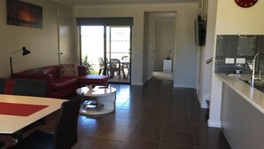 A modern living room with a red sofa, a coffee table, and a dining area with a table and chairs. There is a kitchen area with a sink and a countertop.