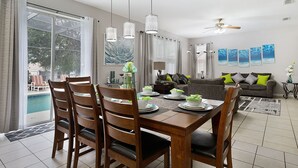 A dining area with a table set for four, a sofa, and a ceiling fan in a well-lit living room.