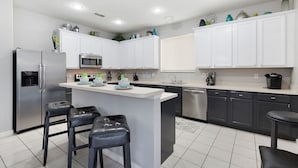 A modern kitchen with white cabinets, stainless steel appliances, and a central island with bar stools.