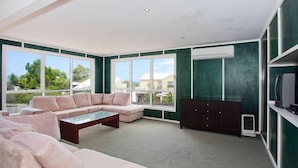 Ein modernes Wohnzimmer mit einer Eckcouch, einem Couchtisch und einem dunklen Schrank. Große Fenster bieten einen Blick ins Freie.