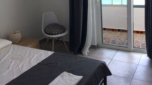 Une chambre avec un lit, une chaise dotée d’un coussin à motifs, un élément décoratif mural et une vue sur l’océan par une porte coulissante.