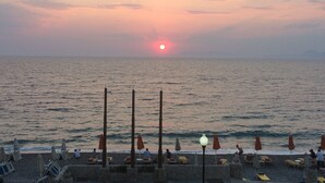 Une plage avec des parasols et des chaises longues, un coucher de soleil en arrière-plan et une mer calme.