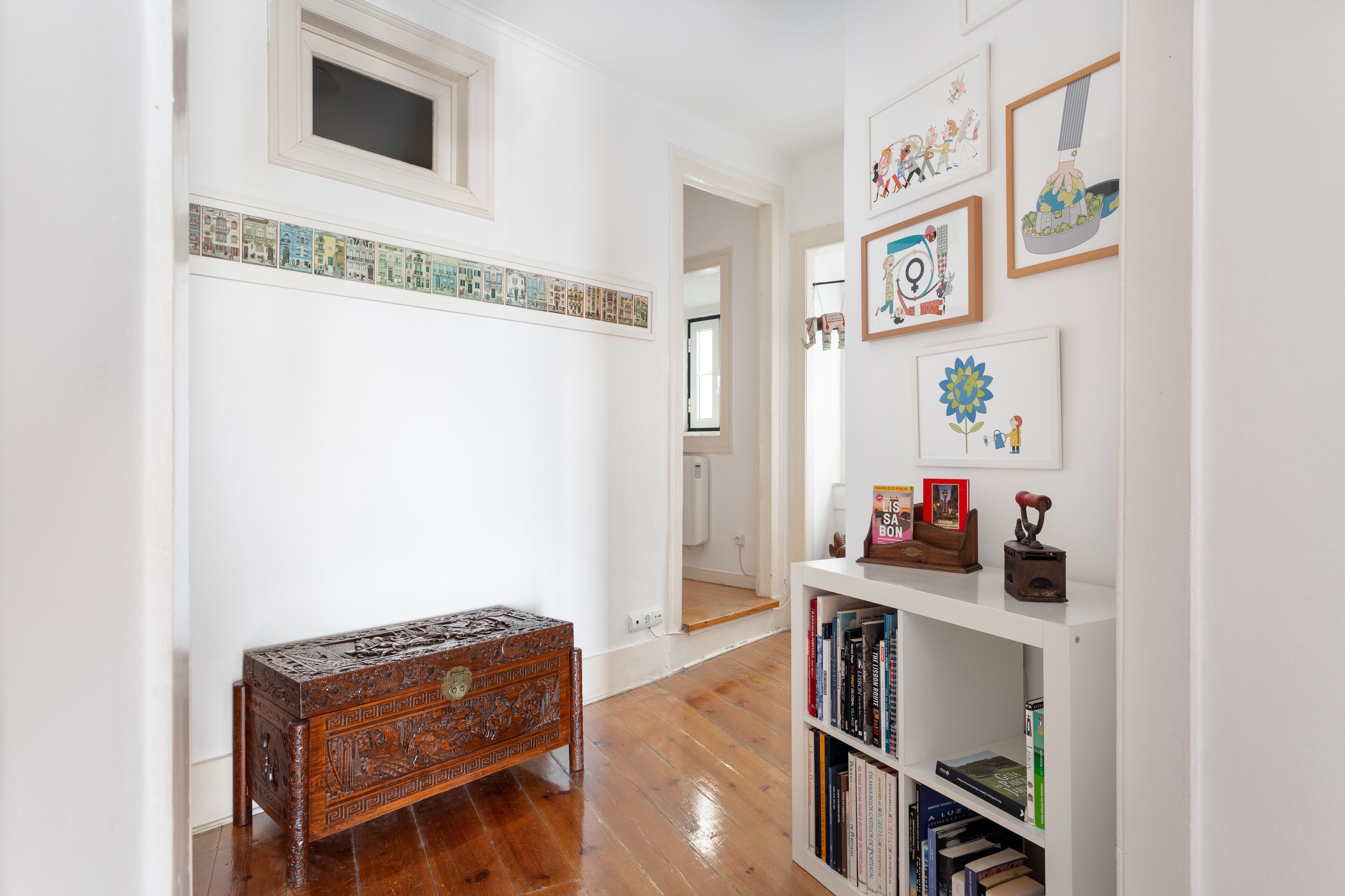 Un couloir avec un banc en bois, une bibliothèque remplie de livres et des œuvres d’art encadrées accrochées aux murs.