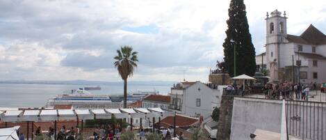 A coastal town with a prominent church, a large ship in the background, and outdoor seating areas.