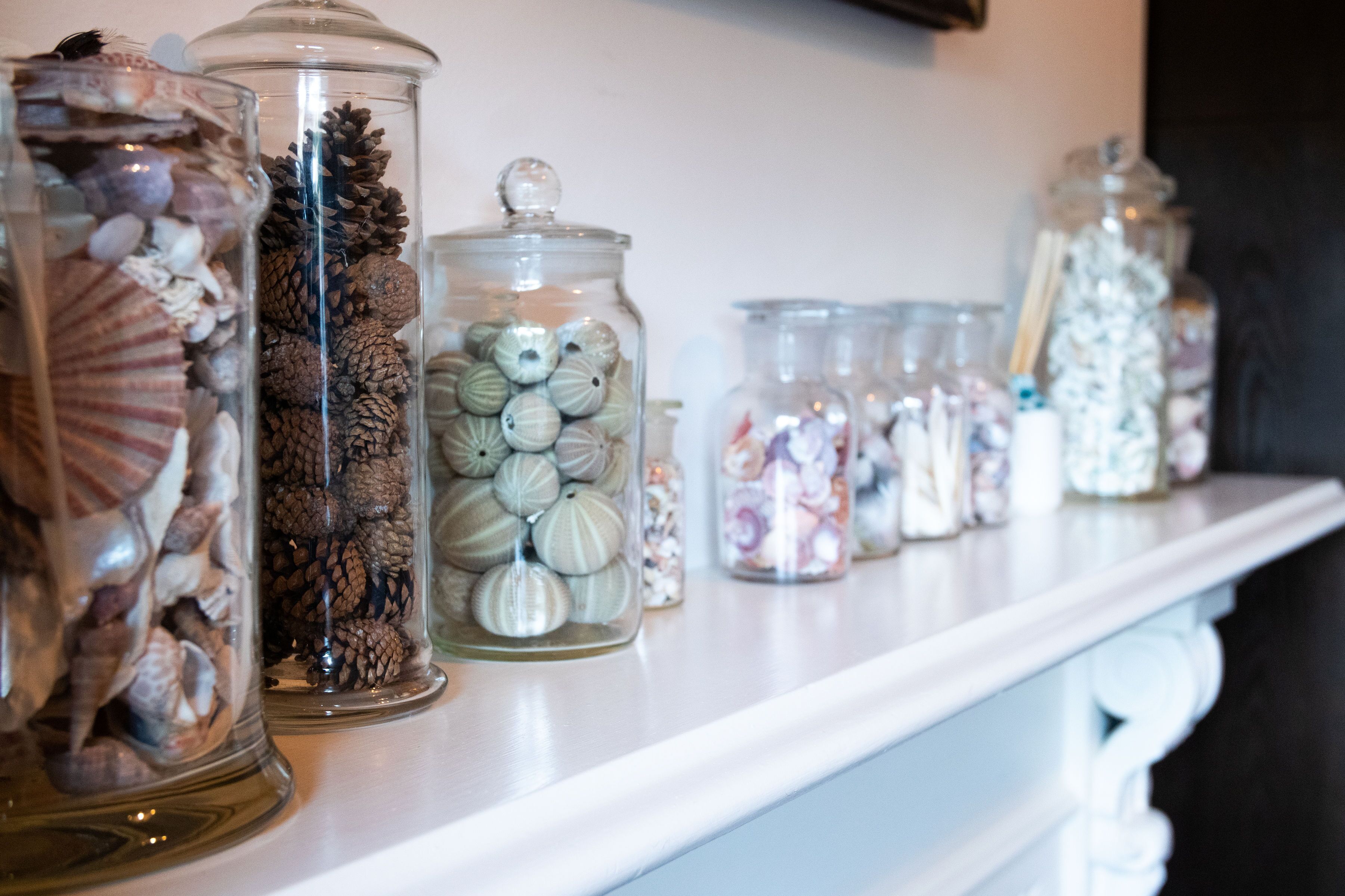 A row of glass jars filled with various decorative items on a white shelf.