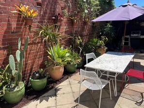 A patio with a table and chairs, surrounded by potted plants and a brick wall. - South Melbourne terrace house.Short walk to Grand Prix,MSAC,Market,Pet friendly (South Melbourne)