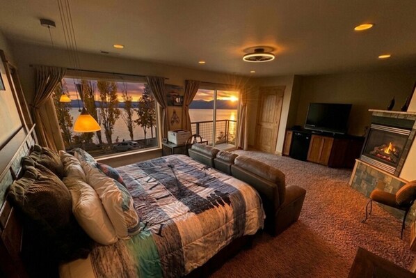 A hotel room with a large bed, a sofa, a TV, a fireplace, and a view of the water.