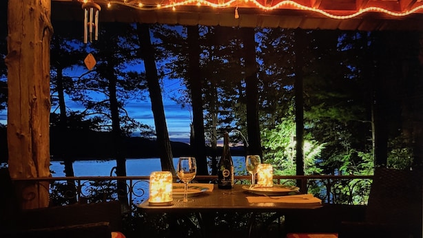 An outdoor dining area with a table set for two, overlooking a body of water and surrounded by trees. - Romantic Lakefront Cabin with Stunning Views (Bridport)
