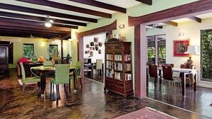 A spacious room with a high ceiling, wooden beams, a large bookshelf, and a dining area with chairs and a table. - Celadon Holiday House @ PALM COVE (Palm Cove)