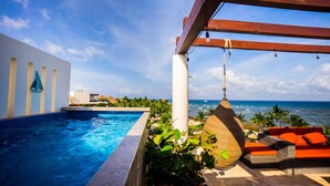 Zona de piscina con vista al océano, una lámpara colgante y mobiliario exterior.