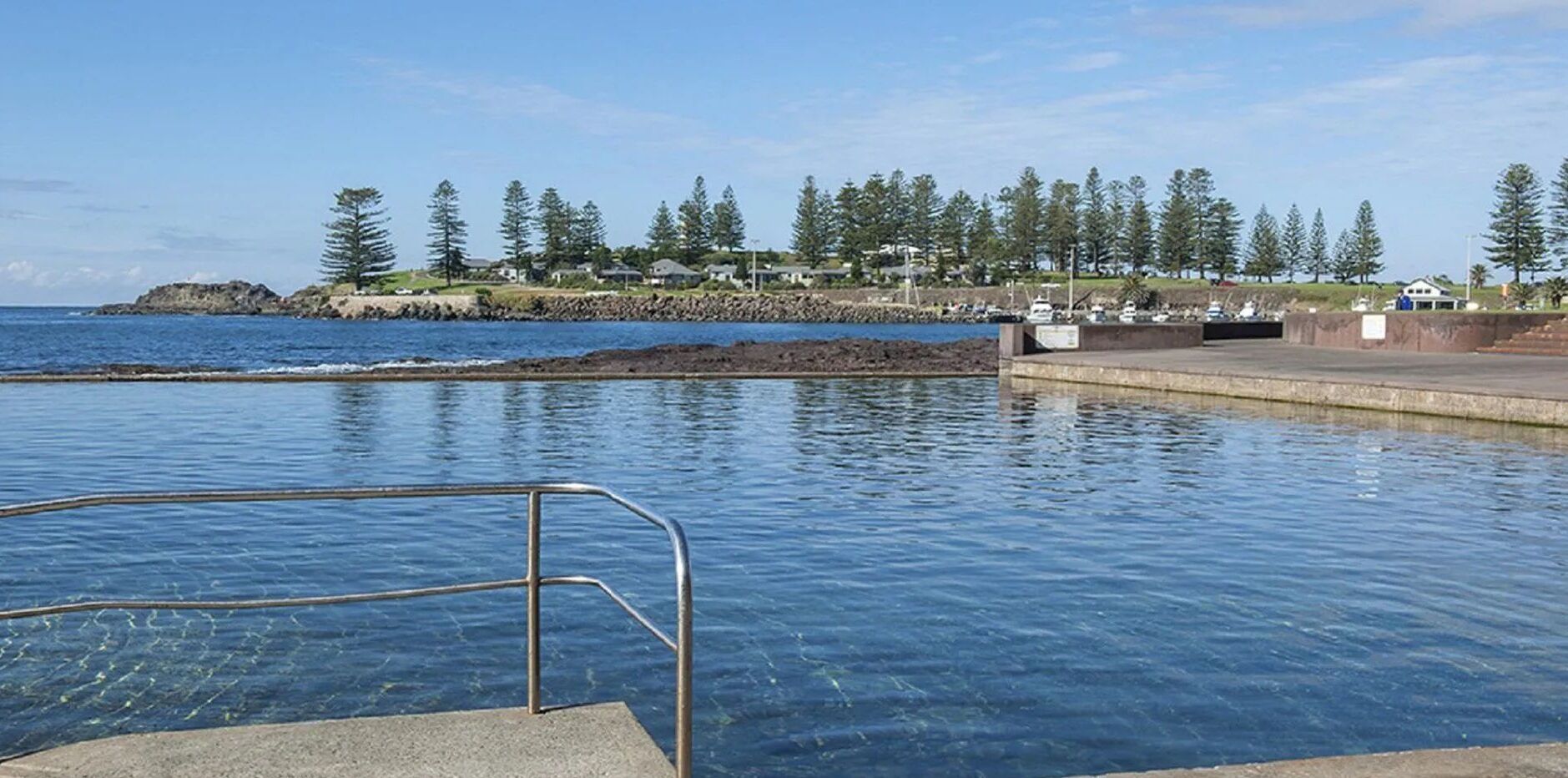 A clear blue pool with a metal ladder leading into the water, surrounded by a concrete deck.