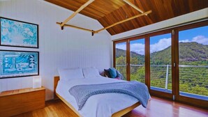 Un dormitorio con una cama grande, suelo de madera, techo de madera y un balcón con vistas panorámicas.