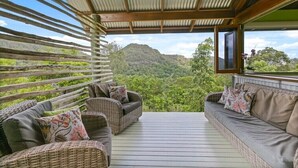 A covered outdoor seating area with wicker furniture and cushions, overlooking a lush landscape. - Off grid tranquillity with beautiful views and no other house in sight (Mapleton)