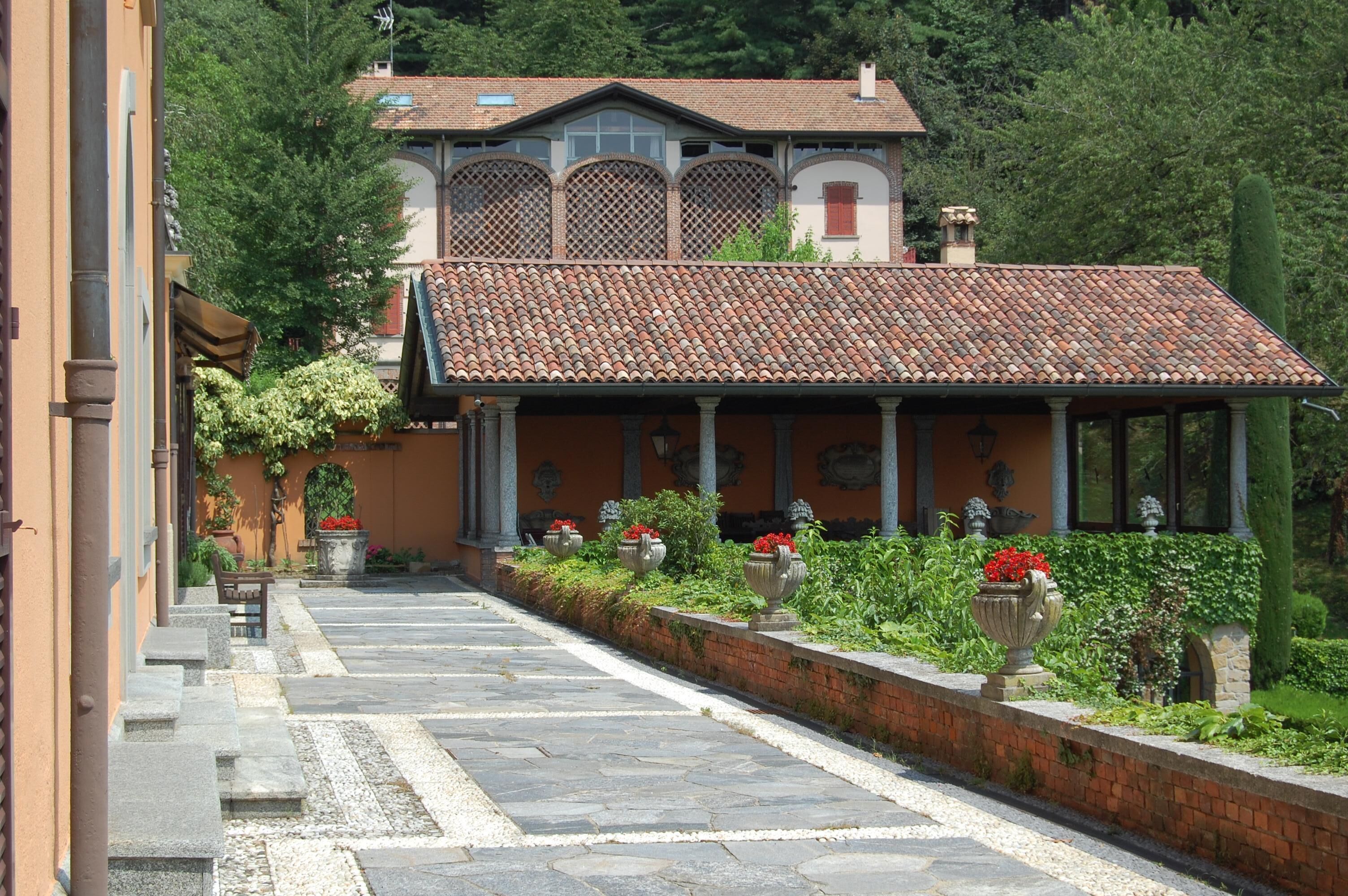 A villa with a tiled roof, a covered walkway, and a garden with potted plants.