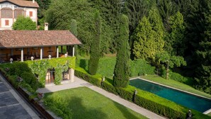 Una villa con piscina, rodeada de jardines cuidados y árboles altos.