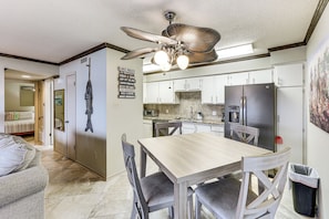 A modern kitchen with a dining area, including a wooden table and chairs, a ceiling fan, and a refrigerator.