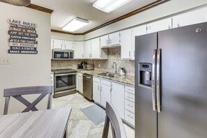 A modern kitchen with stainless steel appliances, white cabinetry, and a granite countertop.