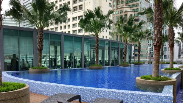 A modern outdoor swimming pool with a tiled edge, surrounded by palm trees and lounge chairs.